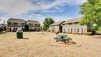 a green picnic table in the middle of a grassy area in front of a row of  at Arbors Of Cleburne, Cleburne, 76033